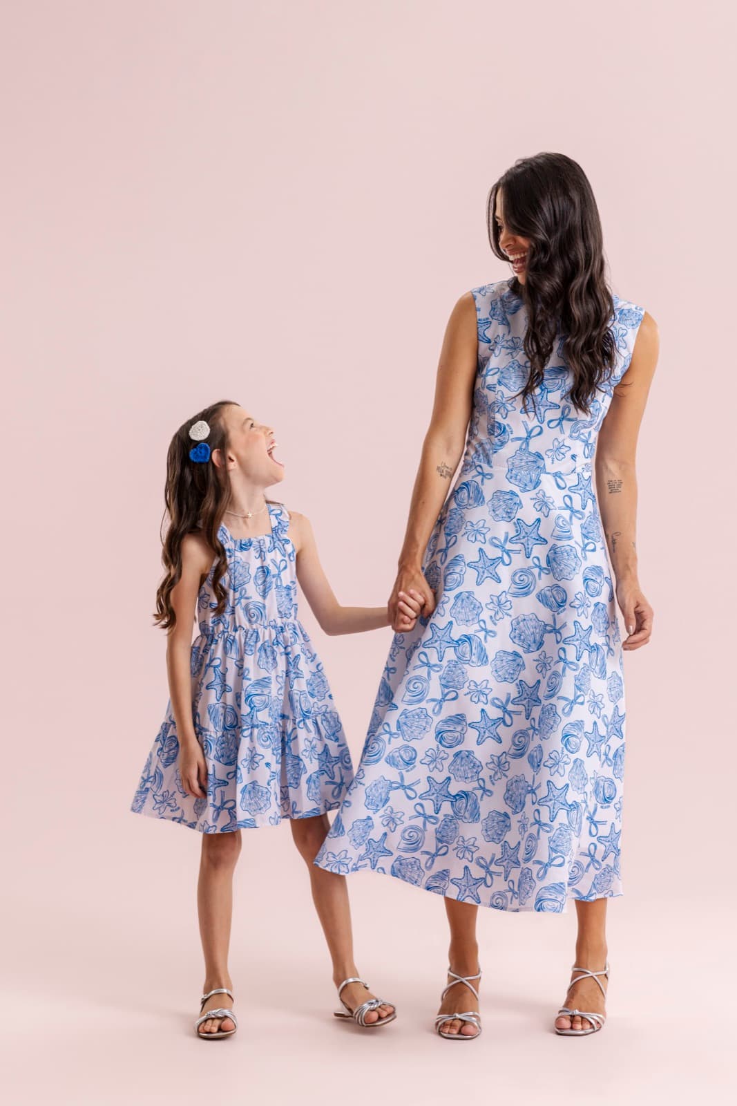 Mãe e filha de mãos dadas usando vestidos com estampa marítima